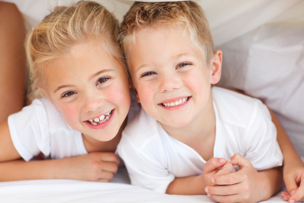 Adorable siblings playing on a bed at home
