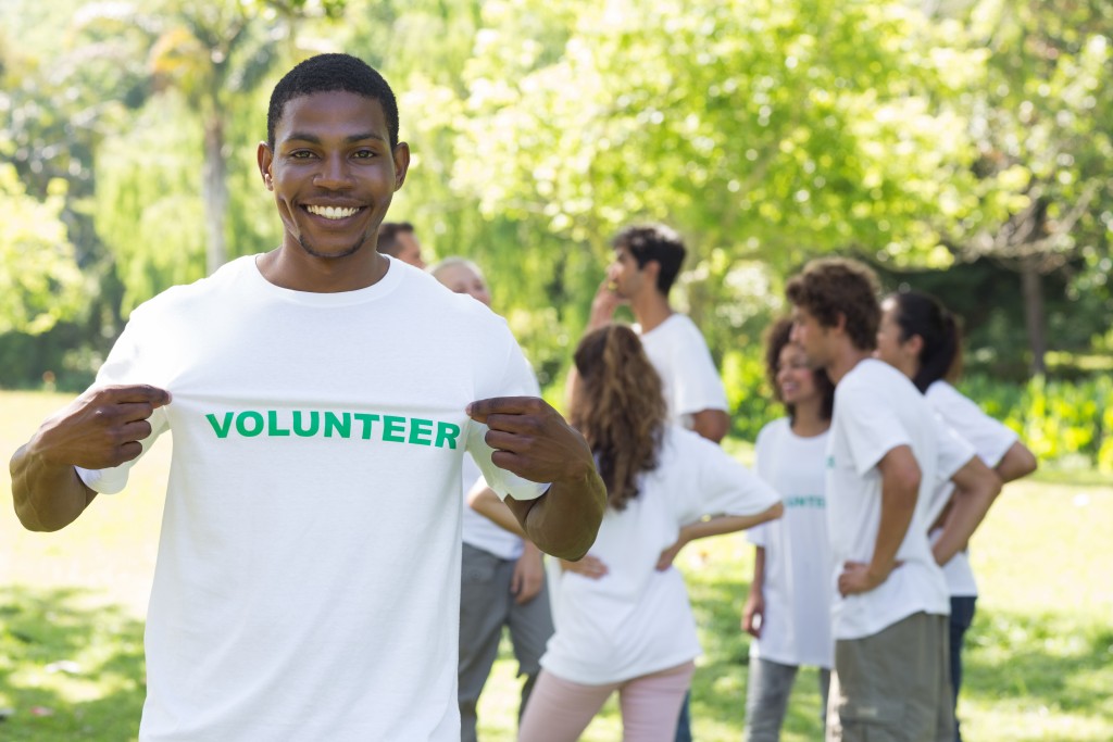 Portrait of happy volunteer holding tshirt with friends disucssing in background
