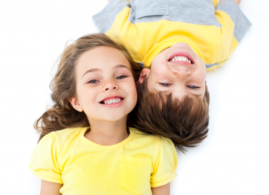 Smiling siblings lying on the floor against a white background