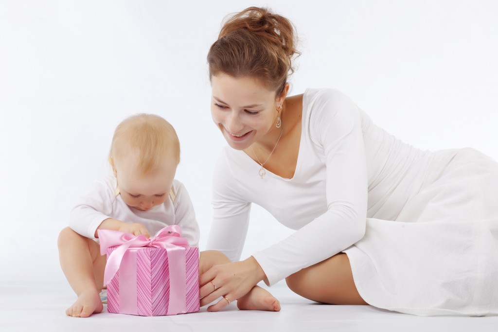 Portrait of mother with her baby opening gift box in white studio