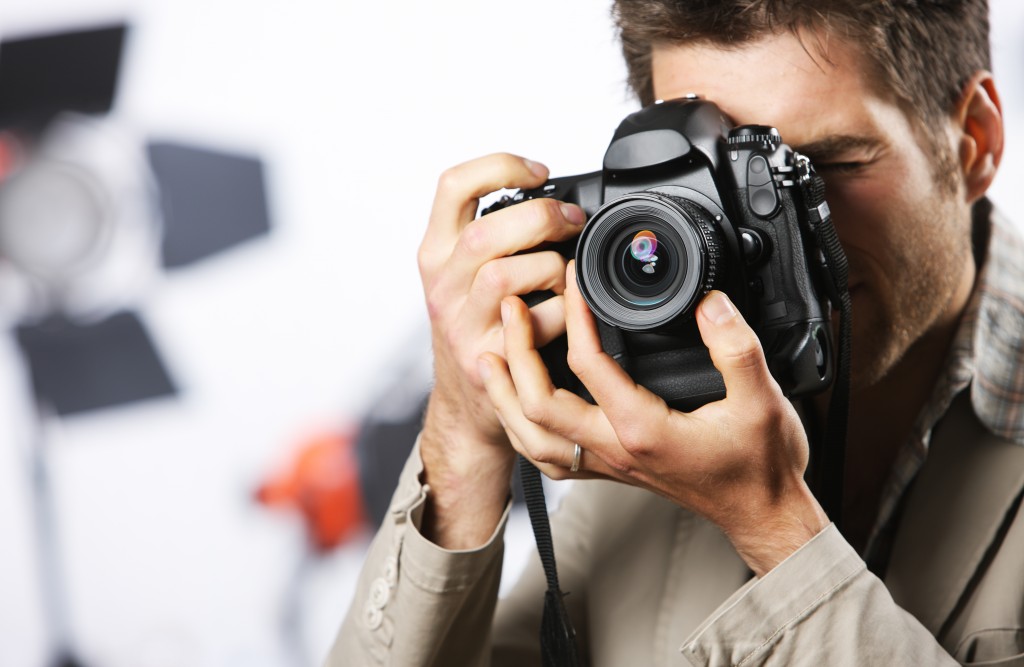 Young man taking photo with professional digital camera, focus on hand and lens