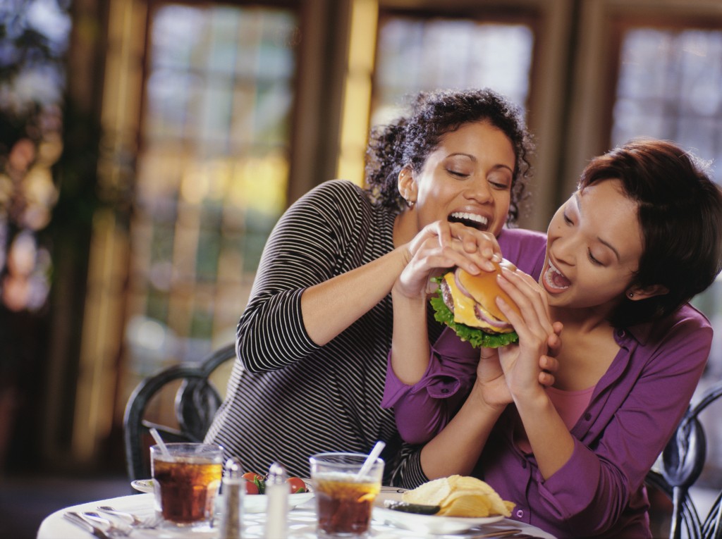Young women fighting to take bite of hamburger