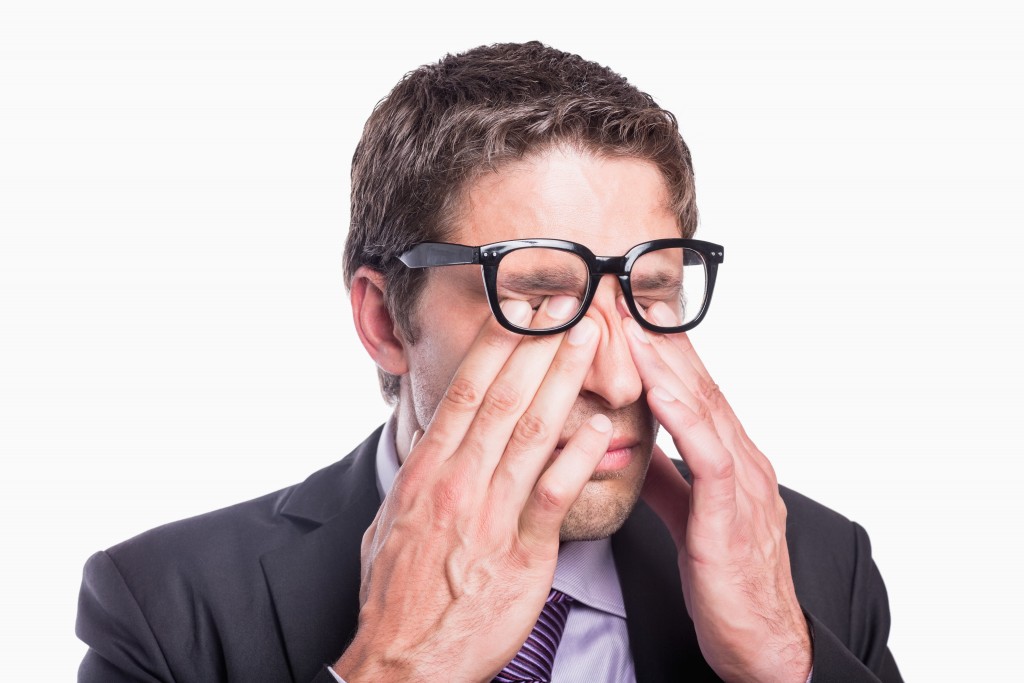 Close-up of a young worried businessman rubbing eyes against white background