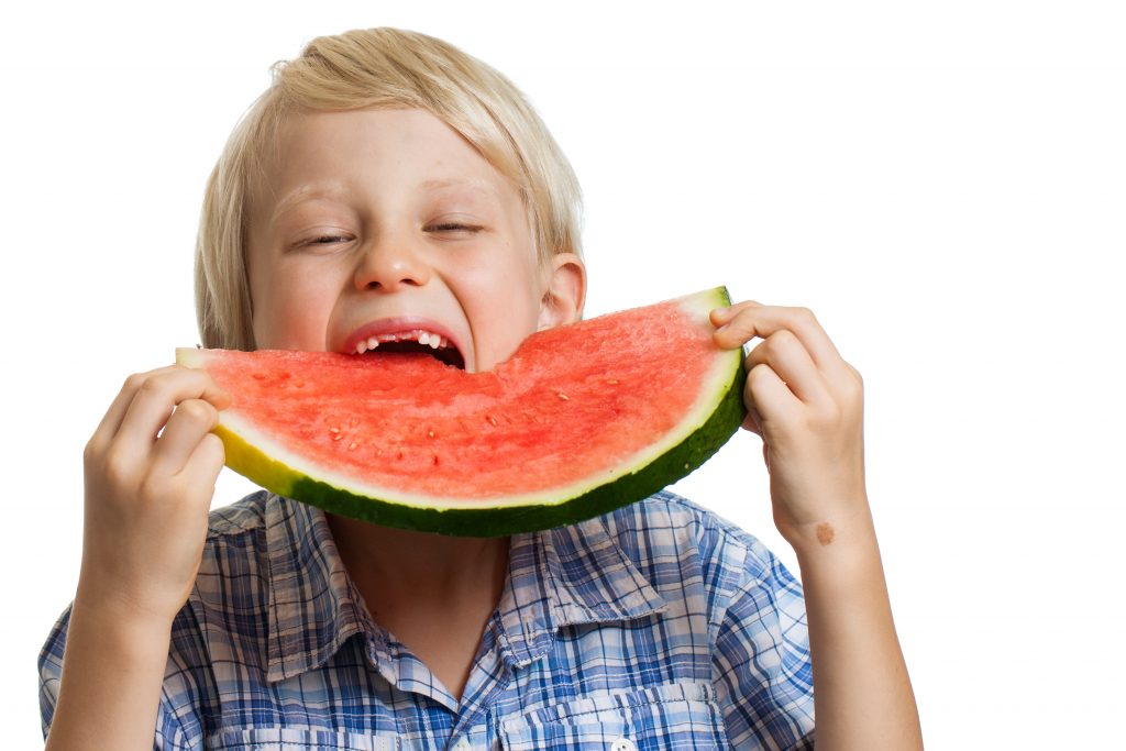 A young boy taking big bite of juicy slice of watermelon. Isolated on white.