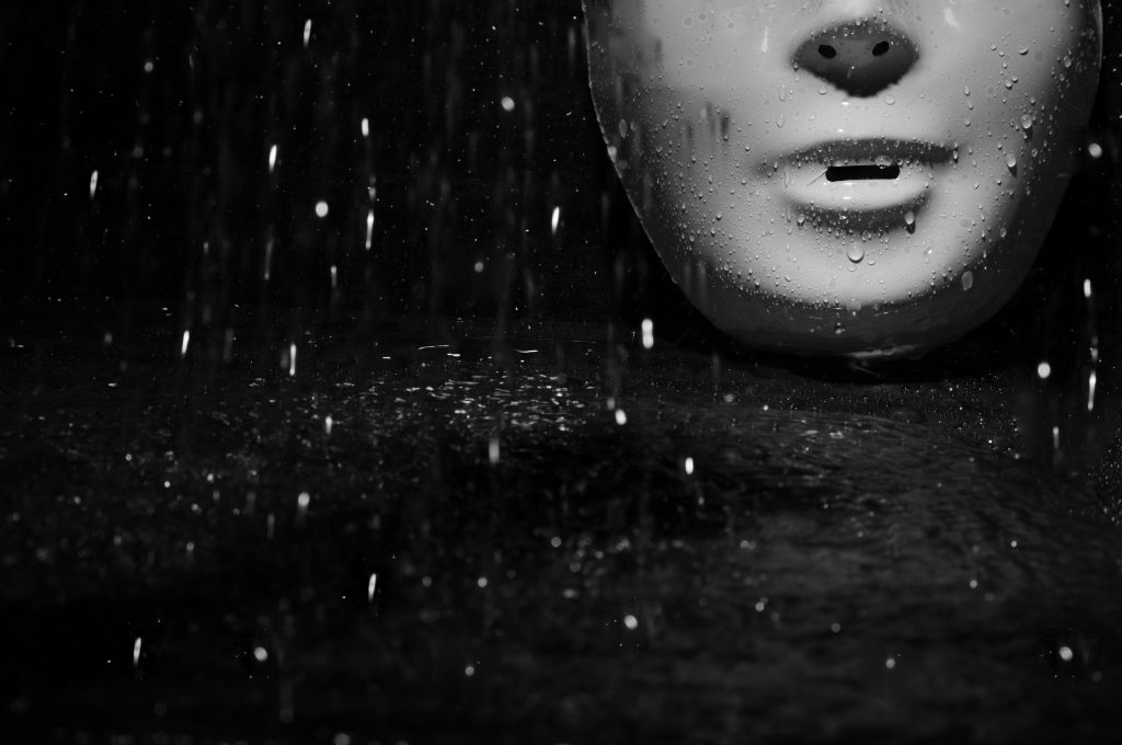 Plastic mask under the rain on a dark background