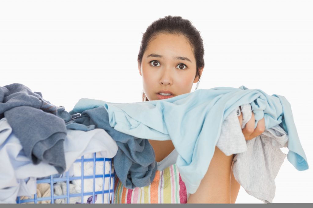 Frowning young woman taking out the dirty laundry from the basket