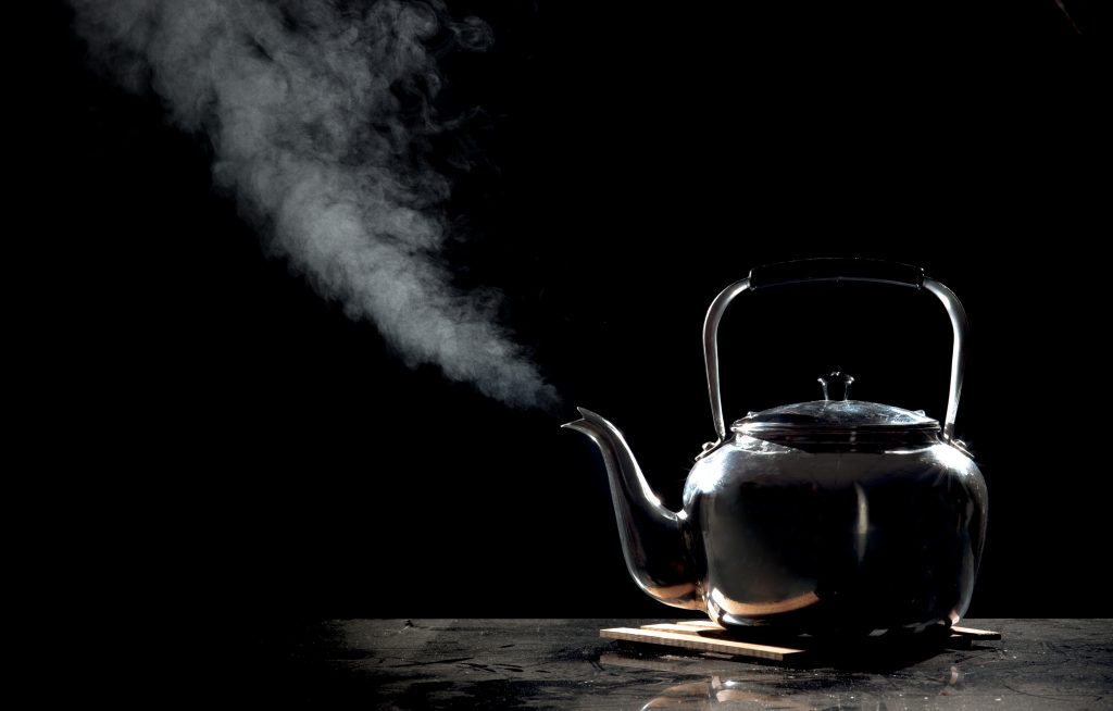 Tea kettle with boiling water on a black background