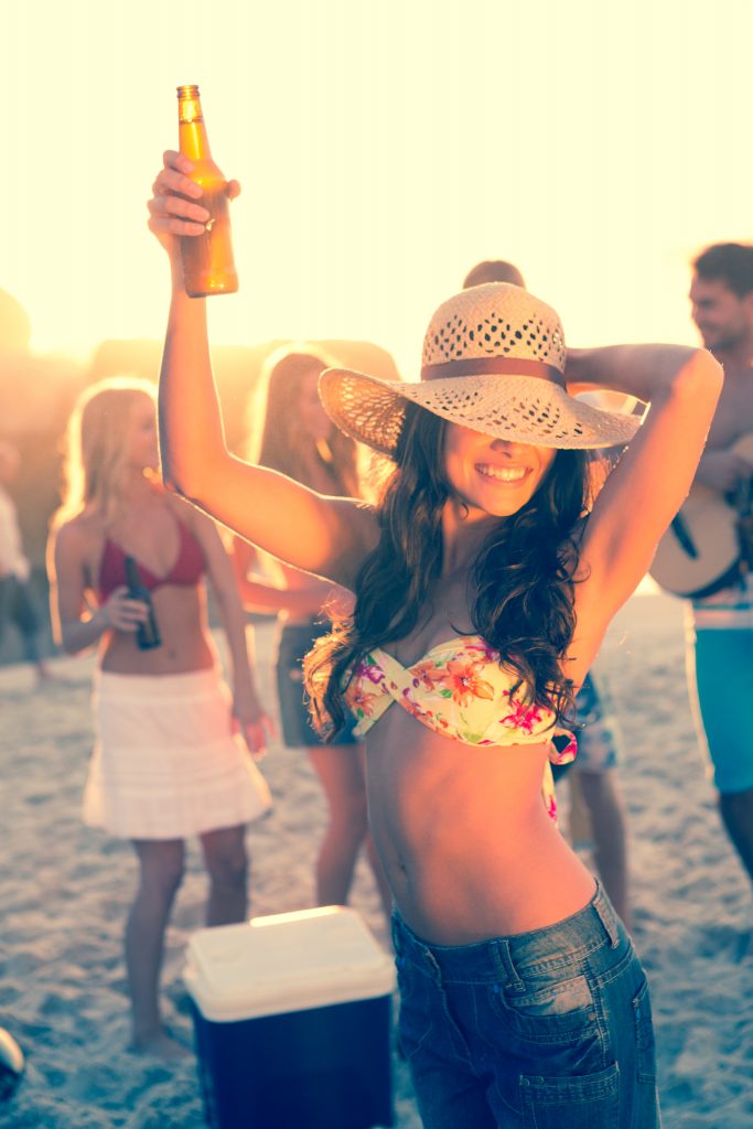 Woman holding beer during a party with her friends on the beach