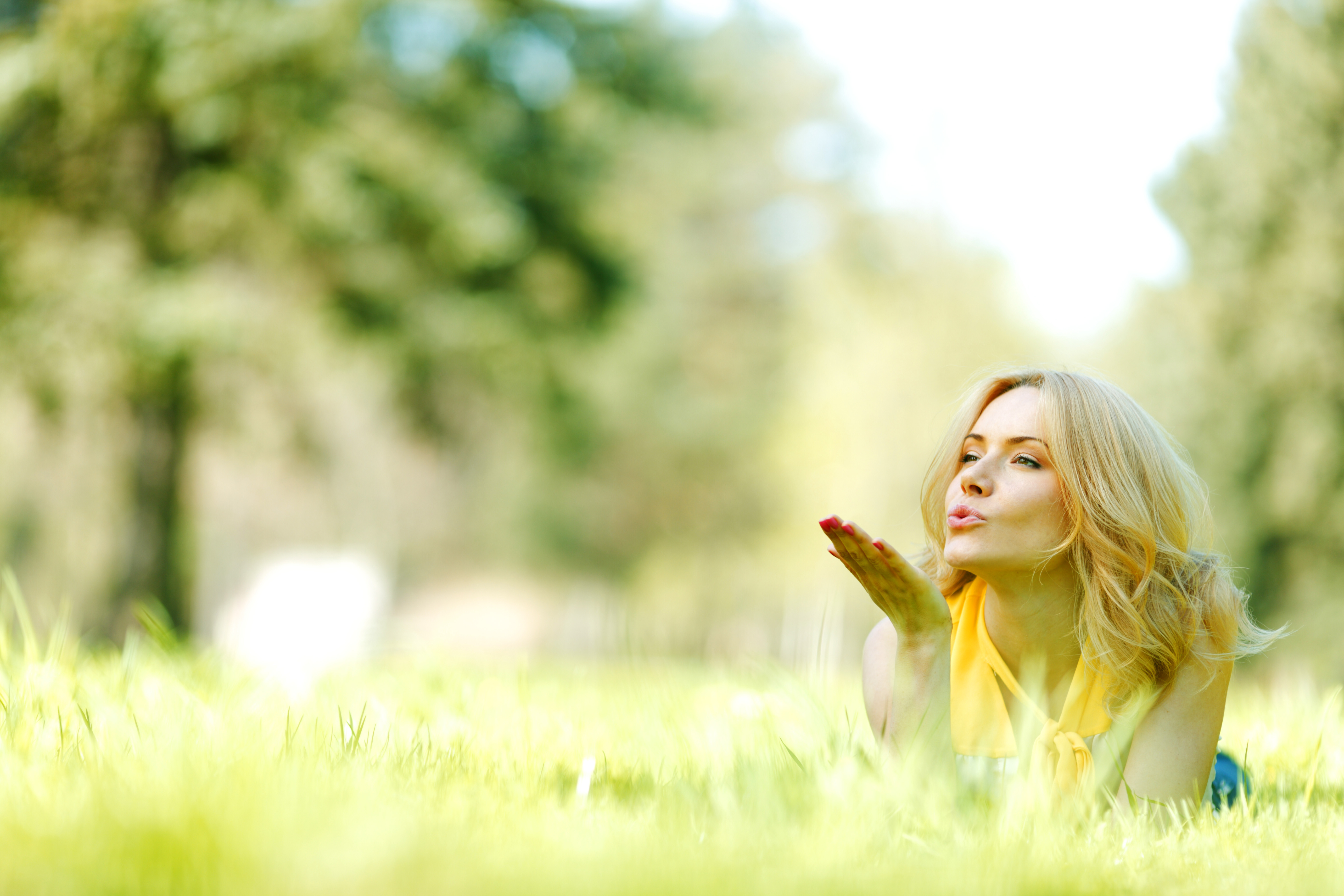 Happy young woman lying on grass and blowing kiss