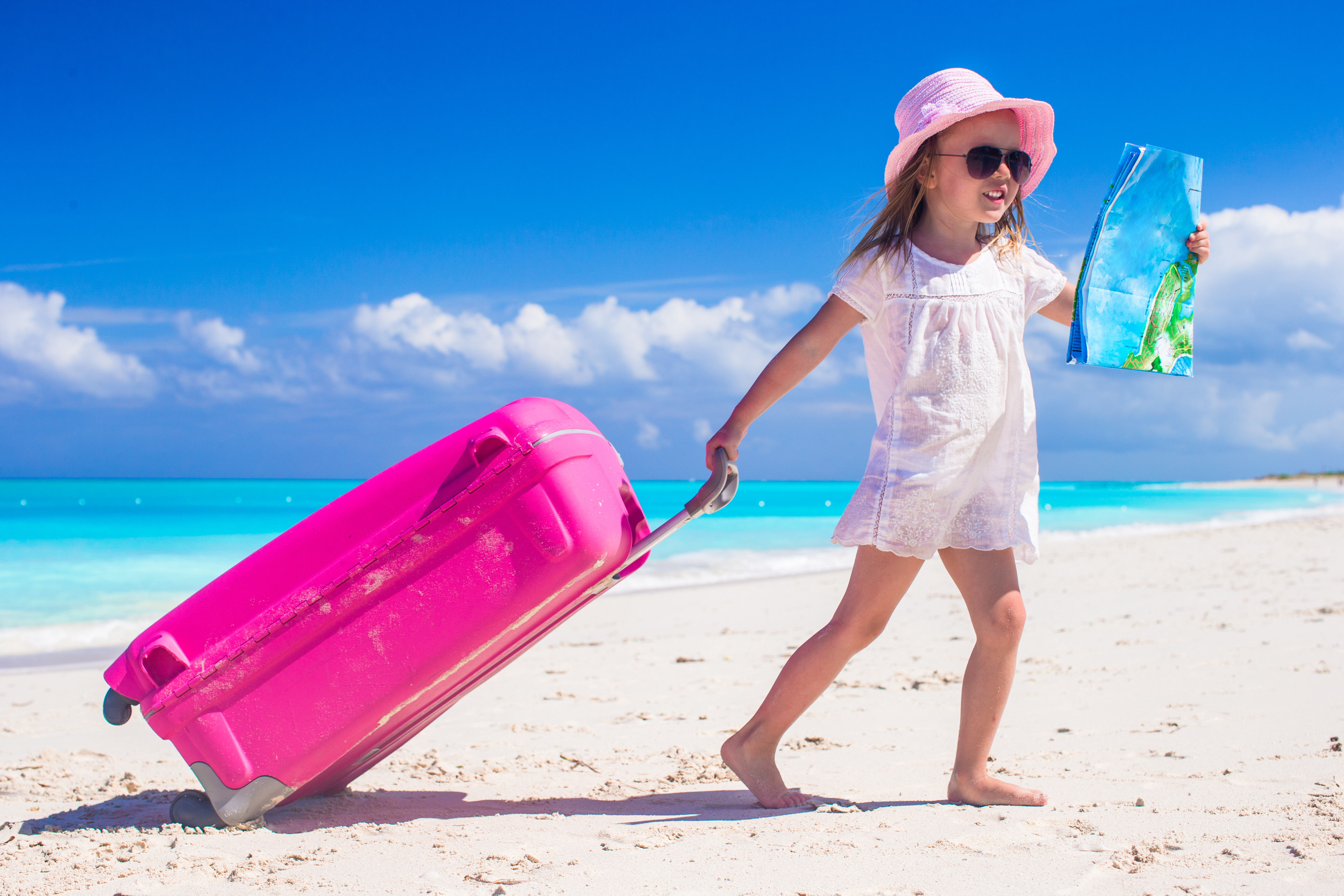 Little cute girls with big suitcase and a map on tropical beach